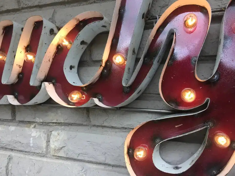 Howdy Metal Wall Decor Lighted NCAA License sign mounted on brick wall, showcasing vintage charm for home or bar décor.