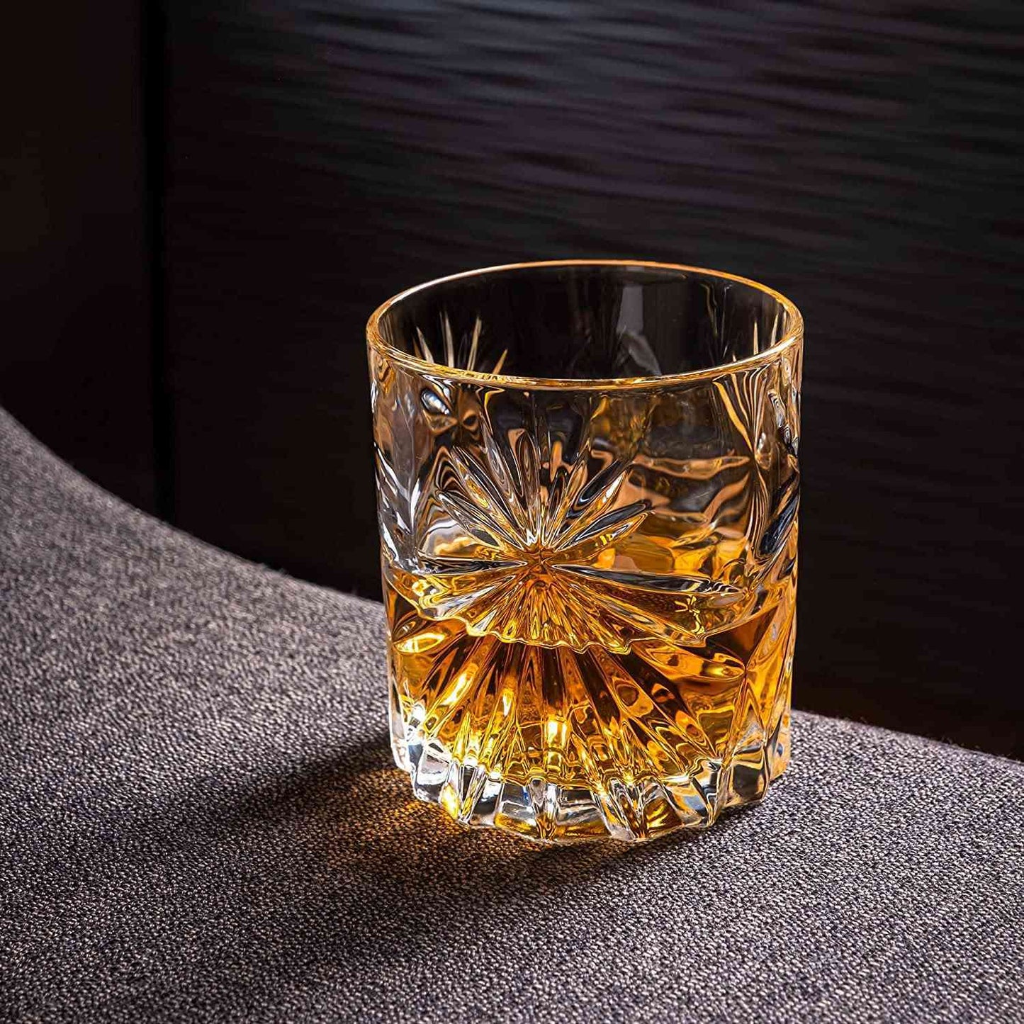 Crystal whiskey glass with amber liquid on textured fabric surface