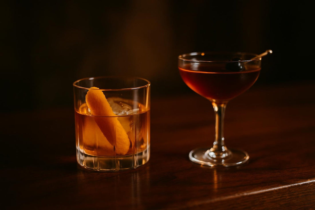 Two classic cocktails side-by-side on dark wood — Old Fashioned comparison hero