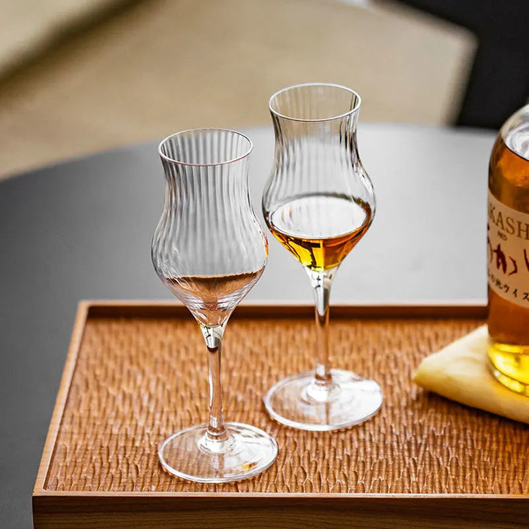 Elegant whiskey tasting glasses with fluted design on wooden tray.