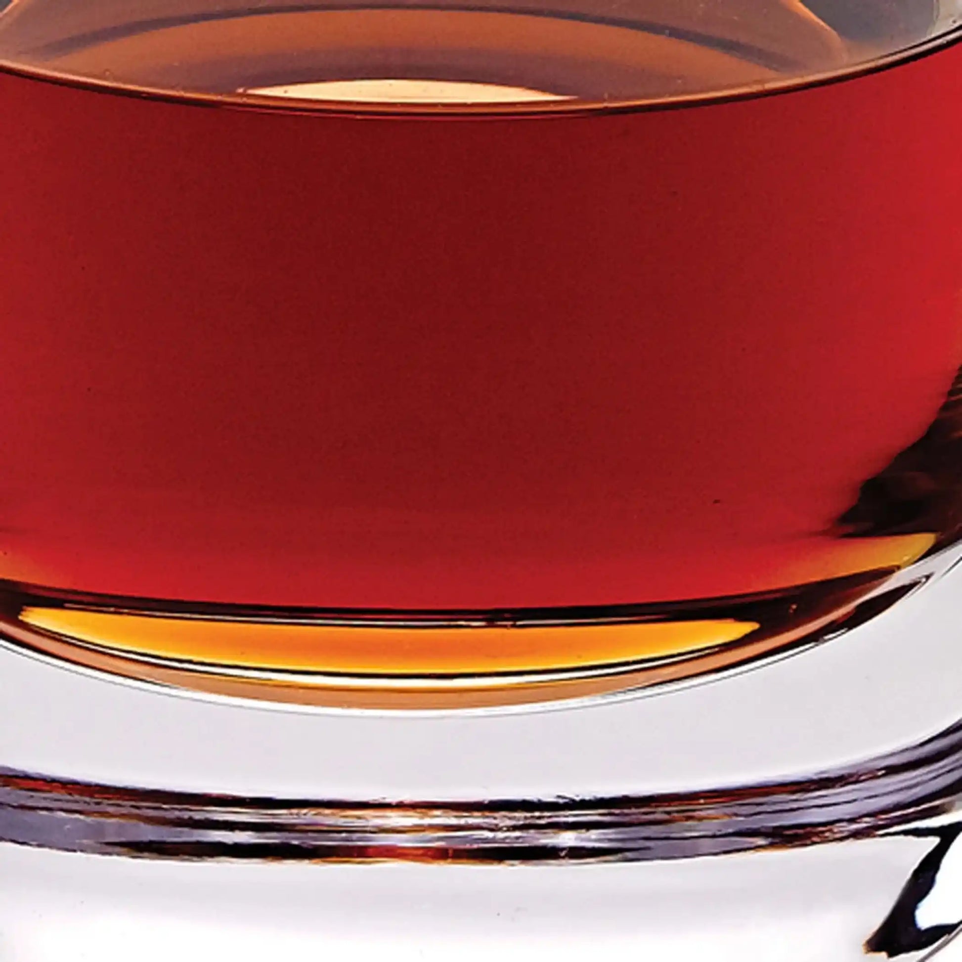 Extreme close-up of the Mouth Blown European Crystal Decanter 28 Oz base with vibrant amber liquid. Perfect for luxury home bar setups.