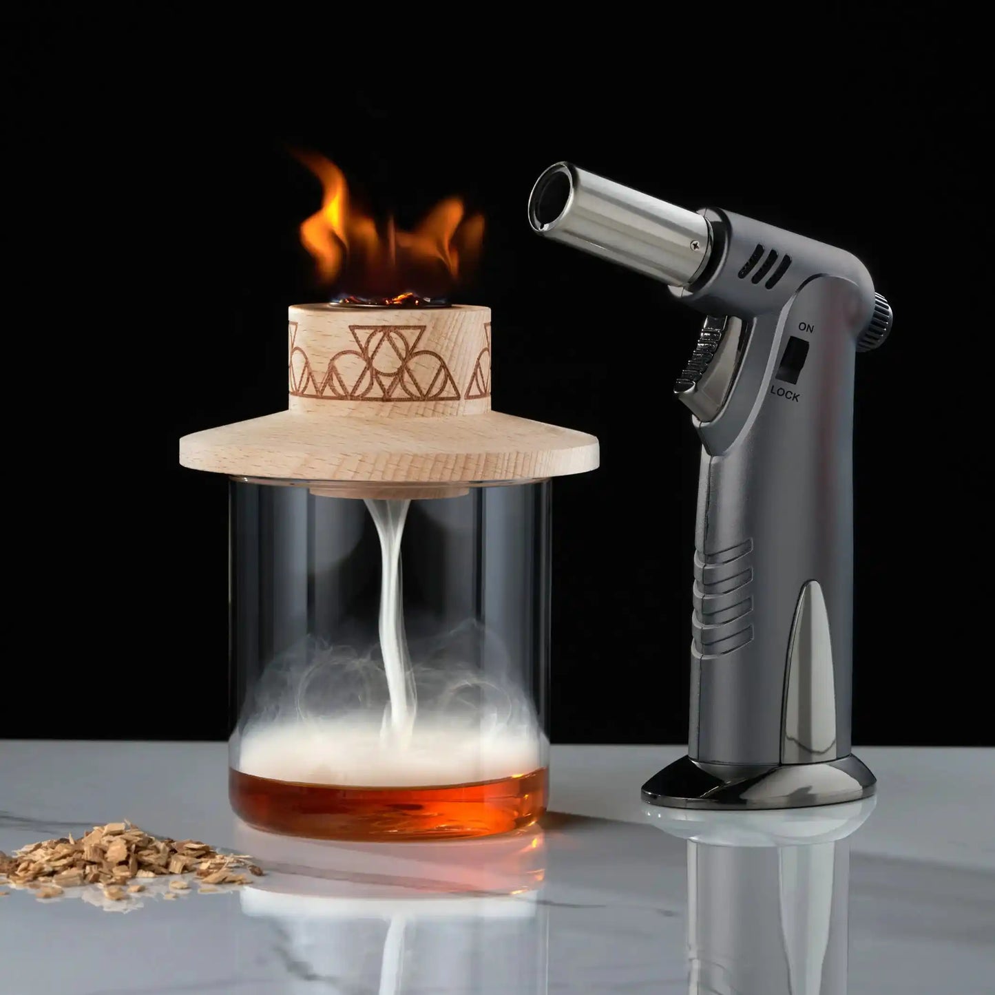 Alchemi Smoker Kit torching wood chips above glass to infuse cocktail with smoke. Premium barware for home mixology and cocktail enthusiasts.