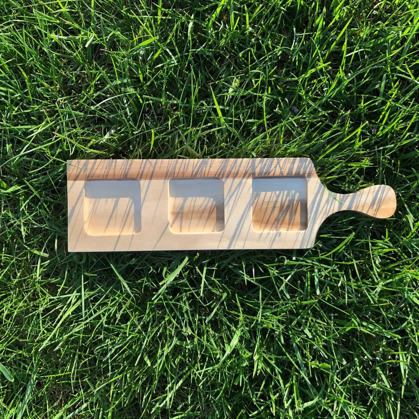 Acacia Flight Board with circular slots and ramekin on grass, highlighting its use for whiskey tastings or creative serving.