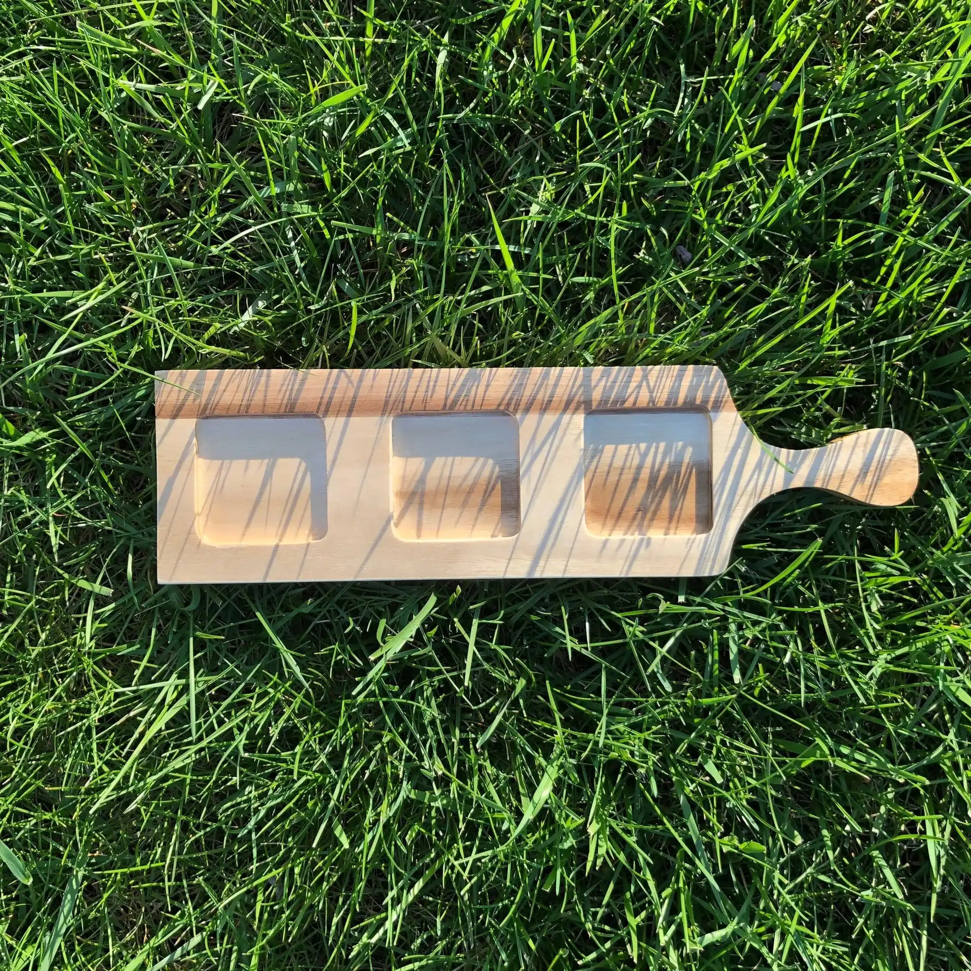 Acacia Flight Board with circular slots and ramekin on grass, highlighting its use for whiskey tastings or creative serving.