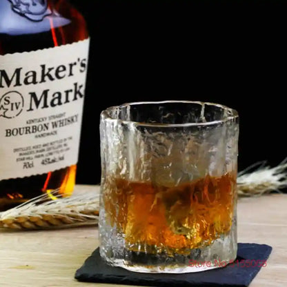 Frosted whiskey tumbler crystal glass with Nordic Japanese design, filled with bourbon beside Maker’s Mark bottle on wooden surface.