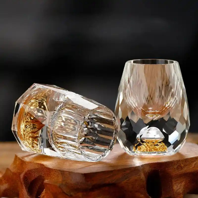 Close-up of two crystal glass liquor cups with faceted design and gold foil mountain base, perfect for upscale home drinkware collections.