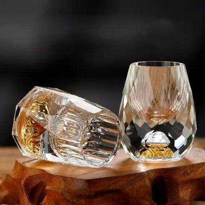 Close-up of two crystal glass liquor cups with faceted design and gold foil mountain base, perfect for upscale home drinkware collections.