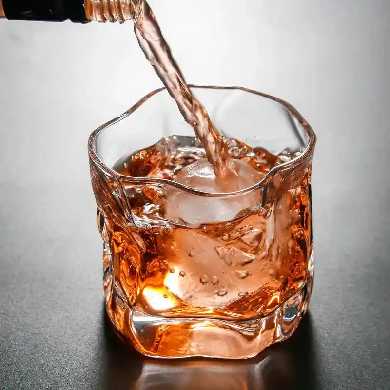 Glass whiskey Japanese style twisted cup being filled with liquor over ice, perfect for home bar and cocktail drink presentation.