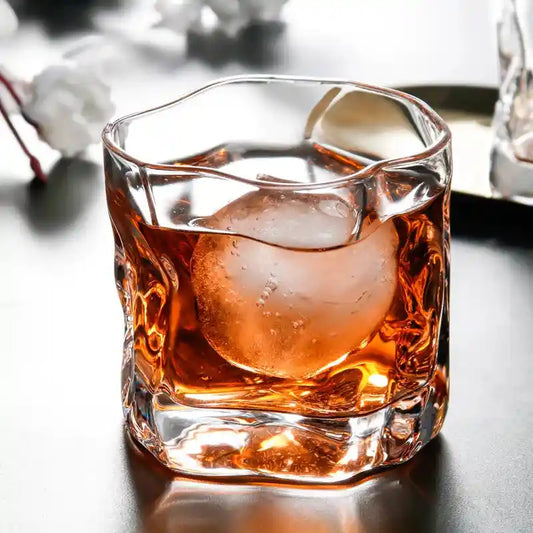 Japanese style twisted whiskey glass with thick base and spherical ice cube, ideal for scotch, liquor, and cocktail drinks at home bars.