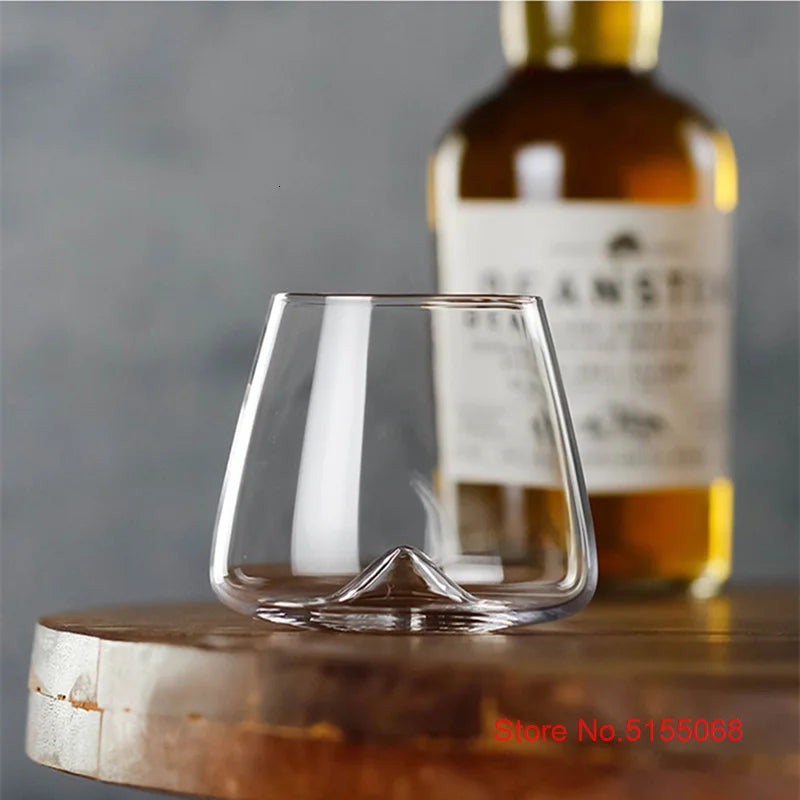 Empty whiskey glass on wooden surface with whiskey bottle behind
